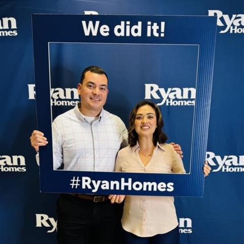Couple celebrating new home purchase with Ryan Homes, holding a 'We did it!' frame