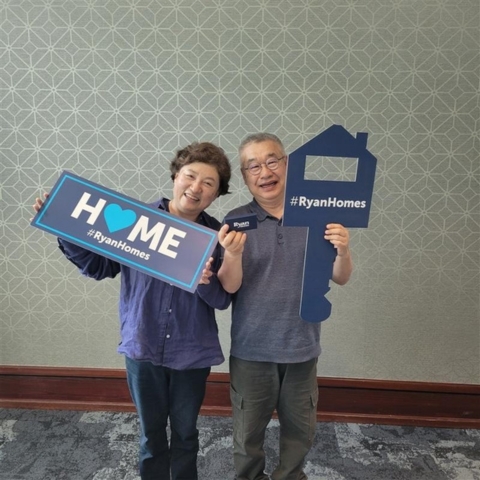 New homeowners celebrating their Ryan Homes purchase, holding branded signs and a key-shaped prop