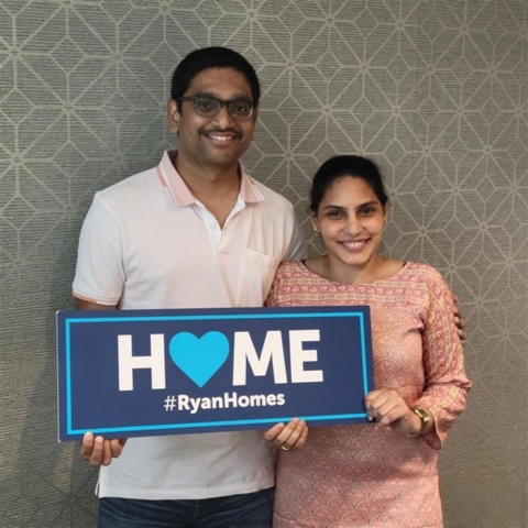 Couple celebrating new home purchase with Ryan Homes, holding a 'HOME' sign