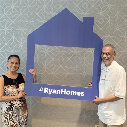 New homeowners celebrating their Ryan Homes purchase, smiling and holding a house-shaped frame