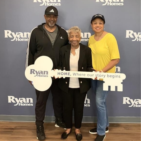 New homeowners celebrating their Ryan Homes purchase, posing with a large key-shaped sign