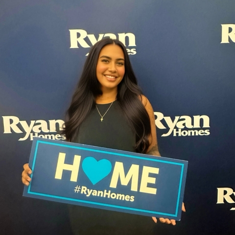 New Ryan Homes buyer celebrating, holding a sign that reads 'HOME #RyanHomes'