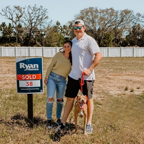 Couple celebrating new Ryan Homes property purchase on lot 38, standing beside 'SOLD' sign